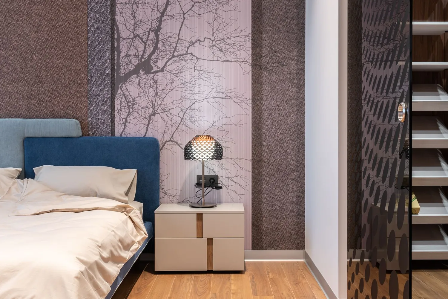 Bedroom with a muted tree-and-branch wallpaper behind a deep blue headboard