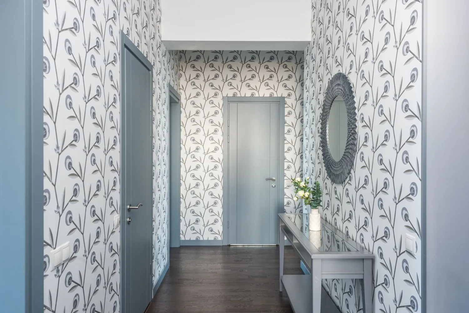 Entry hallway lined with a pale botanical leaf-pattern wallpaper and a round mirror