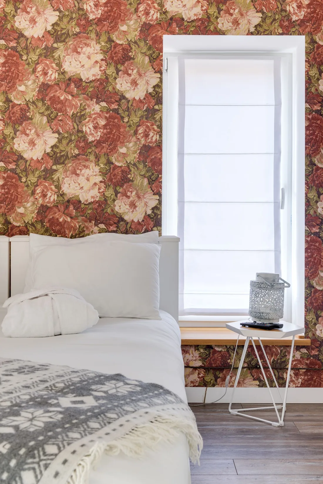 Bright guest room with a red-and-cream floral wallpaper beside the window