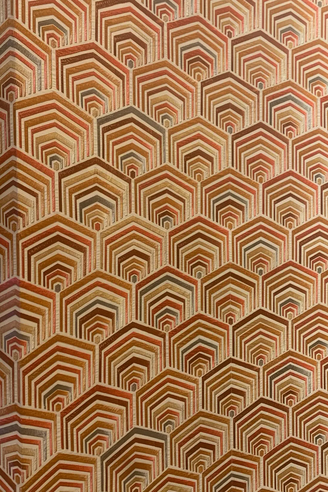 Close view of a copper-toned geometric wallpaper showing its three-dimensional repeat