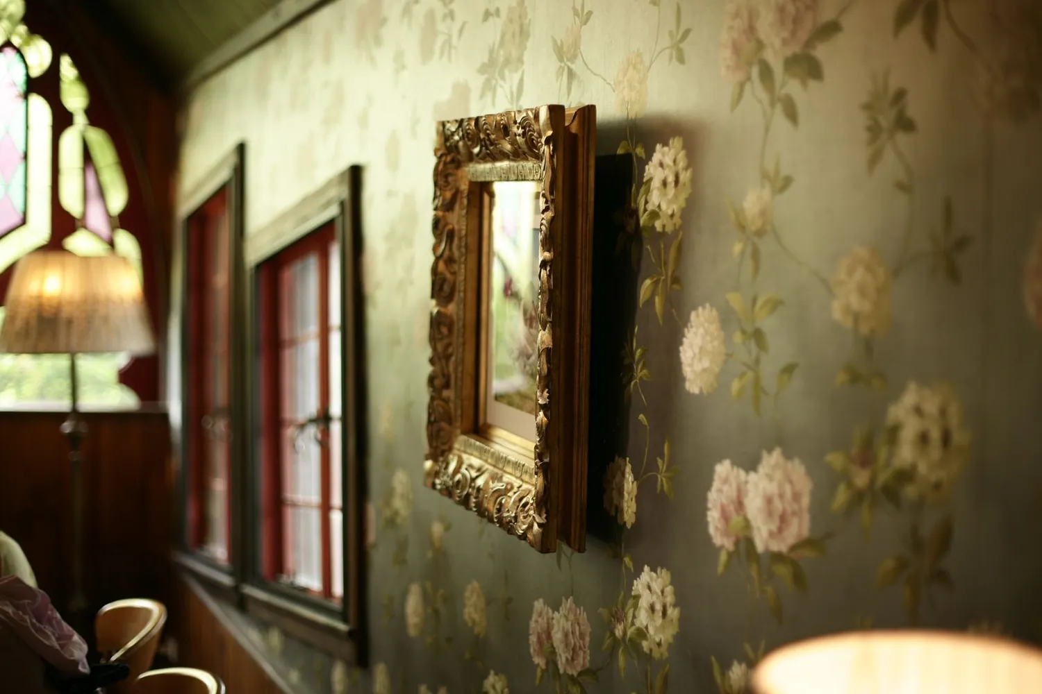 Warm sitting corner with a soft green floral wallcovering and a gilded mirror