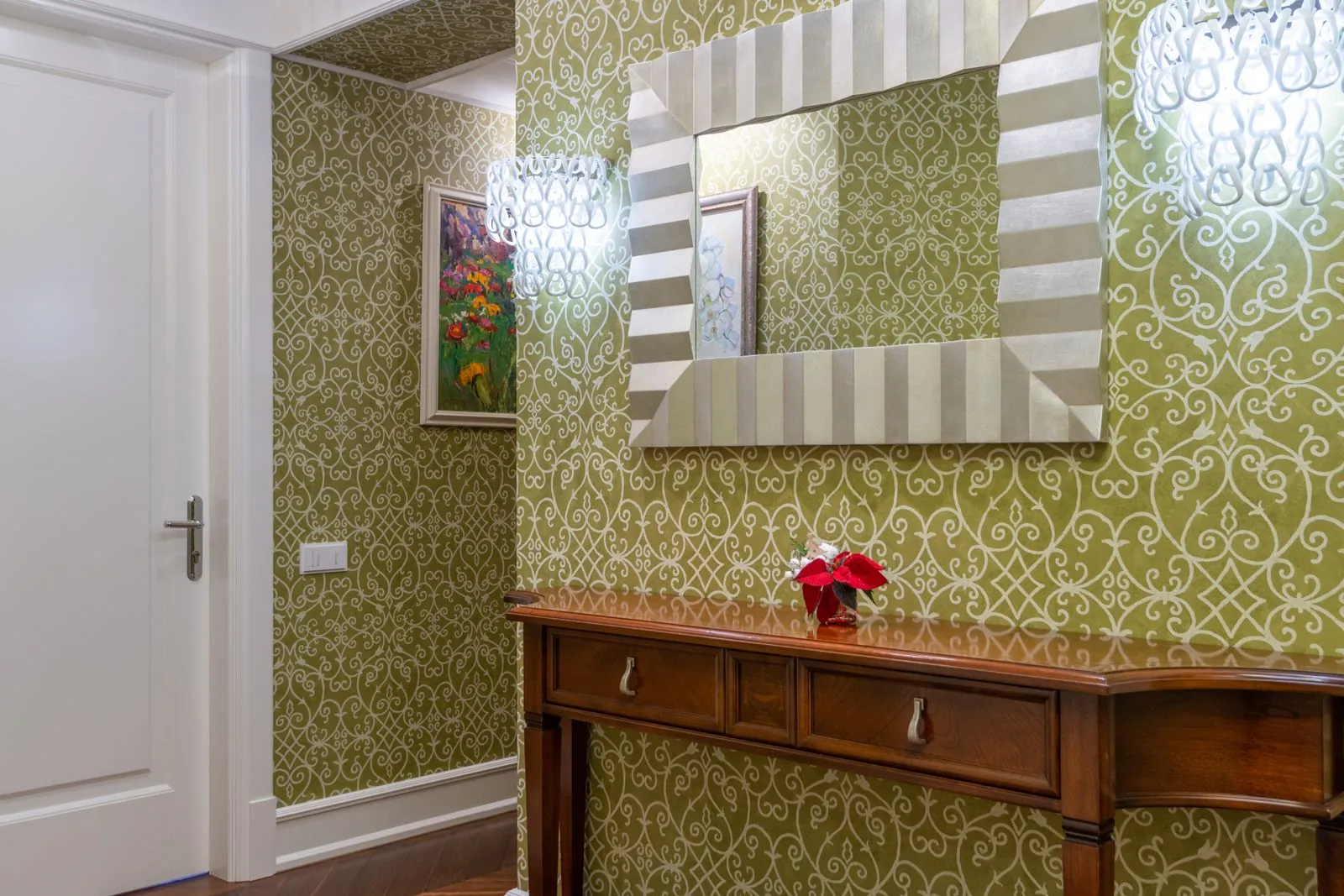 Entry hall with an olive damask wallcovering, a wooden console table, and a framed mirror